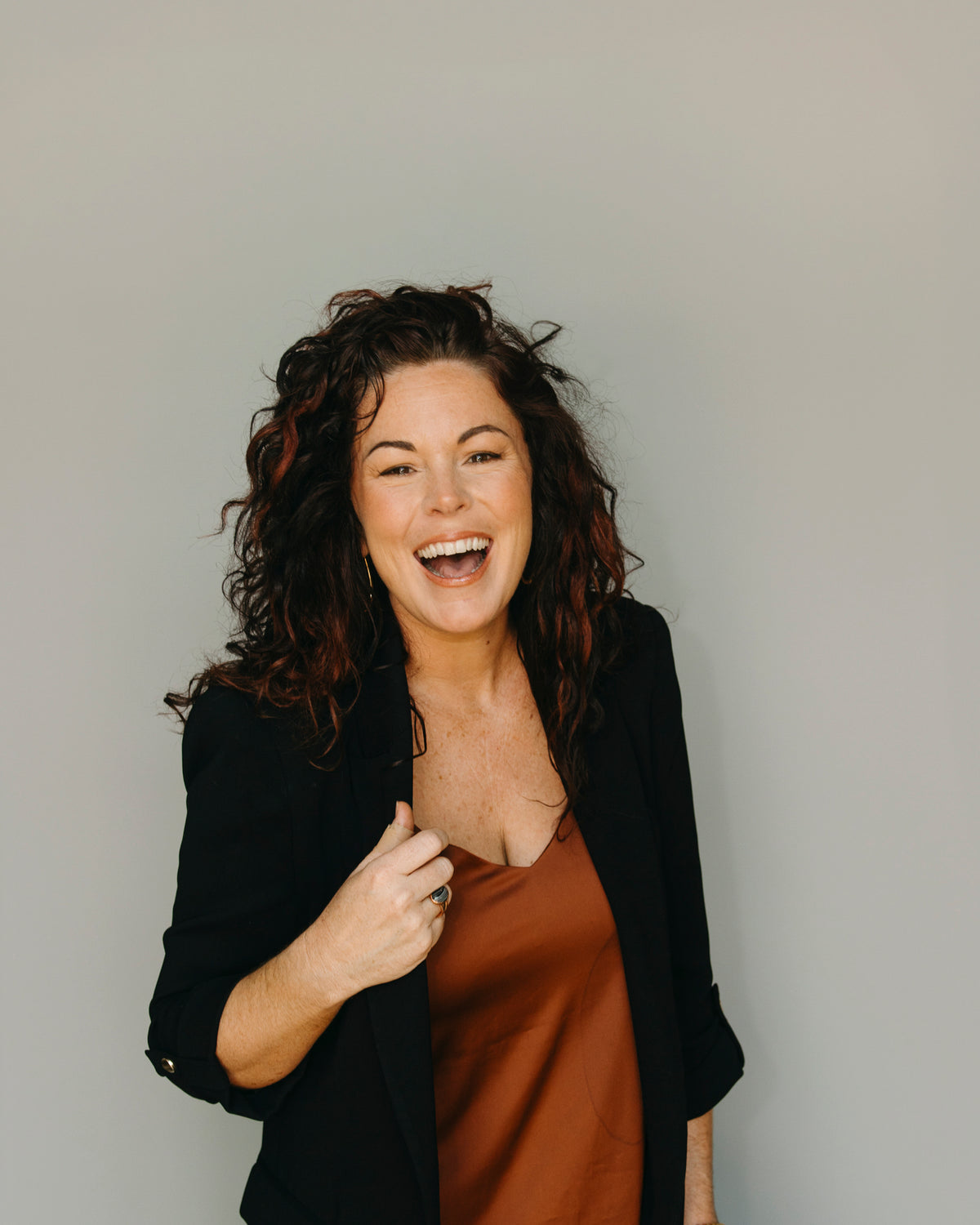 Sabrina Hill, founder of Spice Witch, laughing in a black blazer and rust dress
