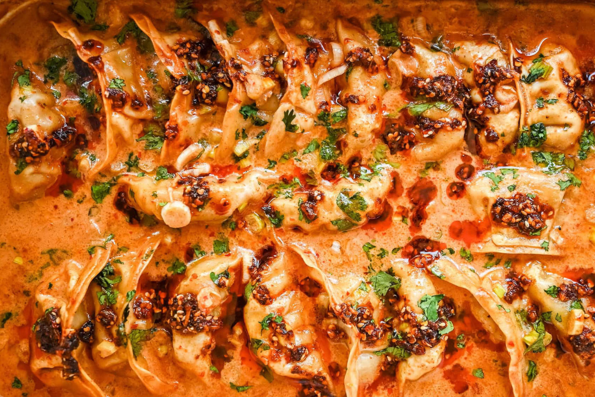 Baking dish of dumplings in creamy coconut curry sauce, drizzled with Spice Witch Black Garlic Chili Crisp and topped with green onions.