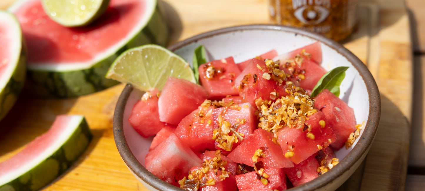 A vibrant bowl of cubed watermelon topped with fresh mint leaves and drizzled with Spice Witch Chili Crisp, showcasing a perfect balance of sweet, cool, and spicy flavors.