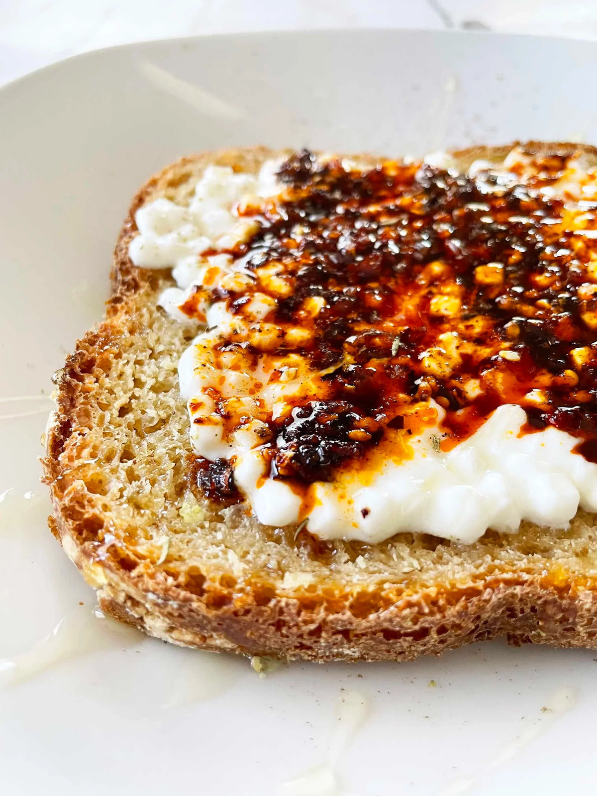Chili crisp spooned over cottage cheese on toasted sourdough with a hot honey drizzle, on a white plate