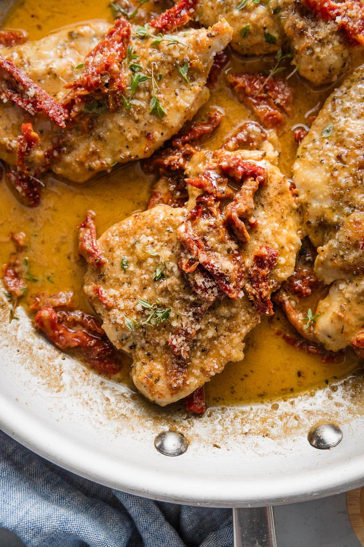 Chicken in a creamy sun-dried tomato sauce in a stainless skillet, topped with parmesan and fresh thyme