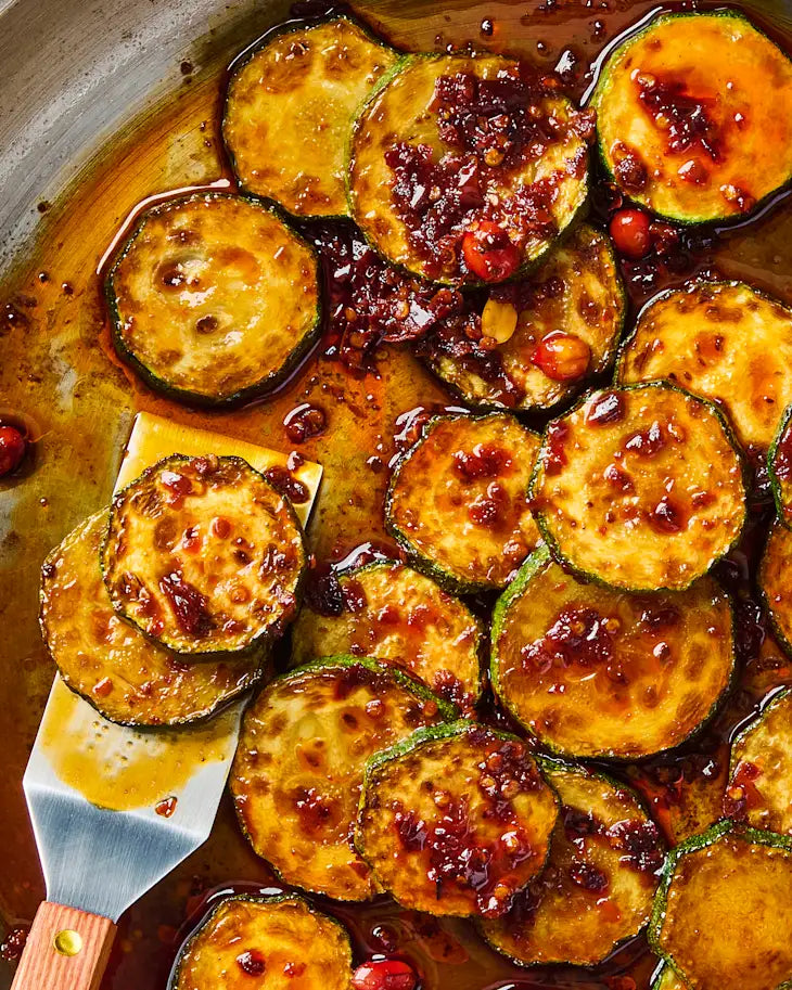 Zucchini coins pan-fried until golden in a skillet, spooned with Spice Witch Chili Crisp and a hot honey glaze