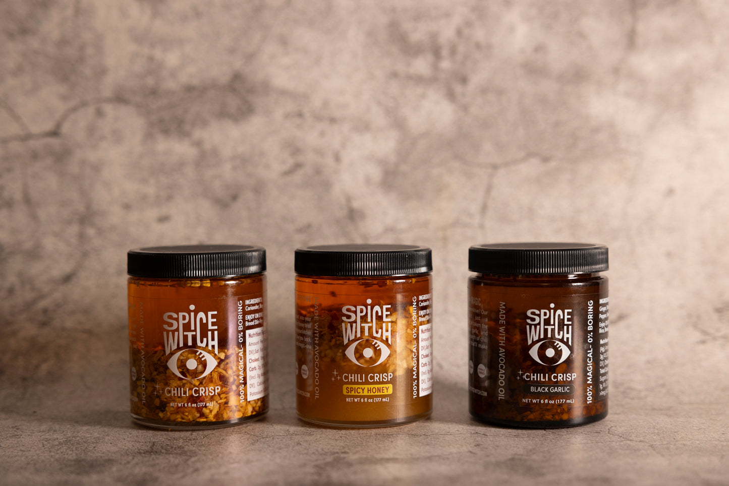 
                  
                    Bundle of Spice Witch Chili Crisp jars displayed with vibrant, spicy ingredients like chili peppers, garlic, black garlic, and a drizzle of spicy honey, highlighting the bold and flavorful textures of the product
                  
                