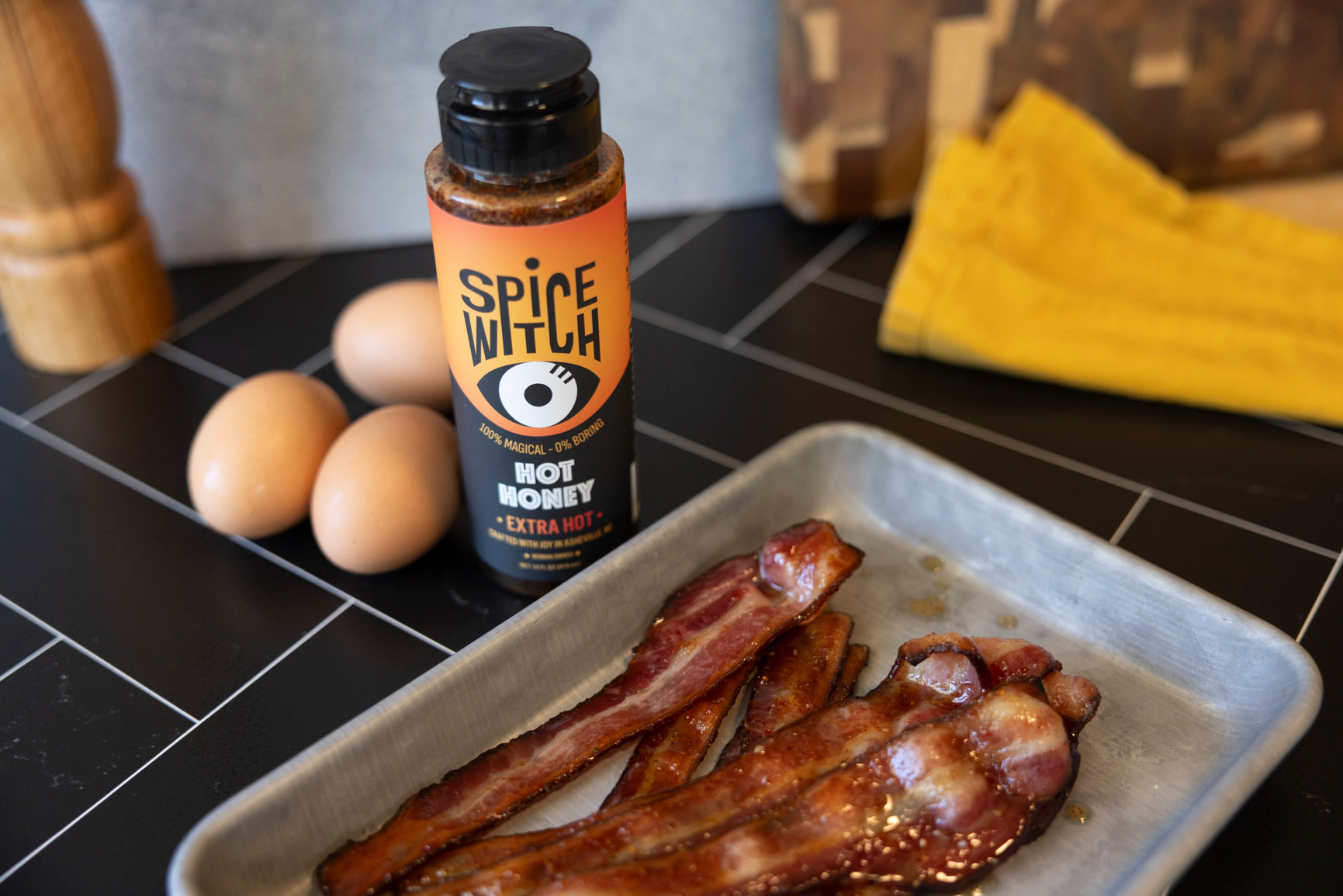 Candied extra hot honey bacon on a sheet pan next to a bottle of Spice Witch Extra Hot Hot Honey